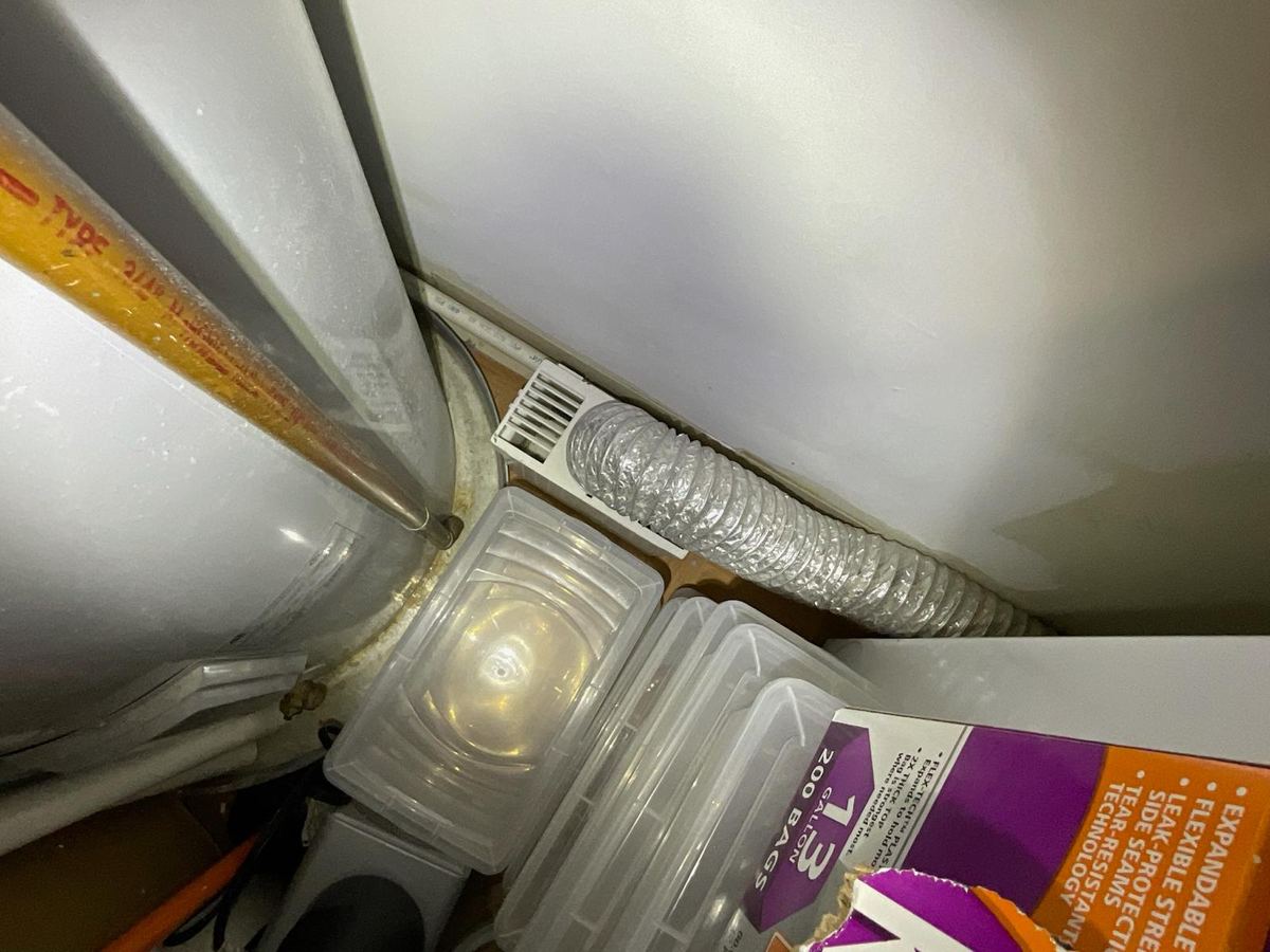 Rusted fittings at the top of a water heater in a crowded utility closet, next to a dryer vent duct