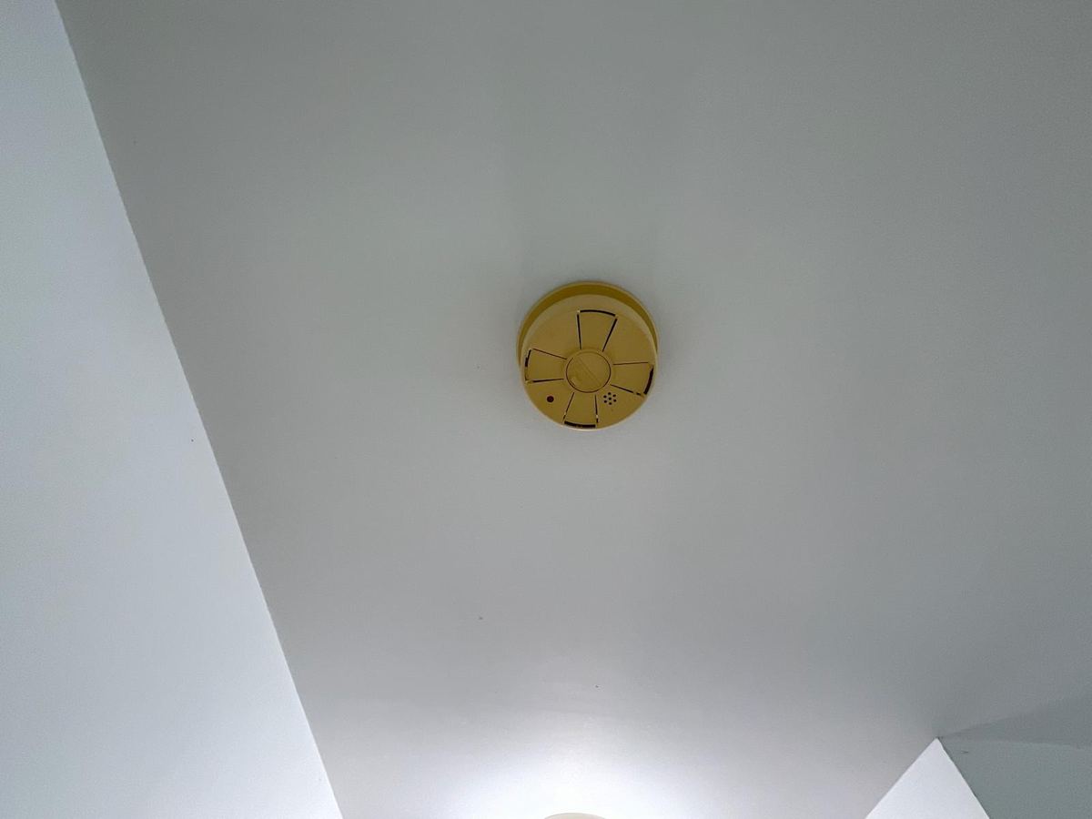 A ceiling-mounted smoke alarm whose white plastic housing has yellowed with age